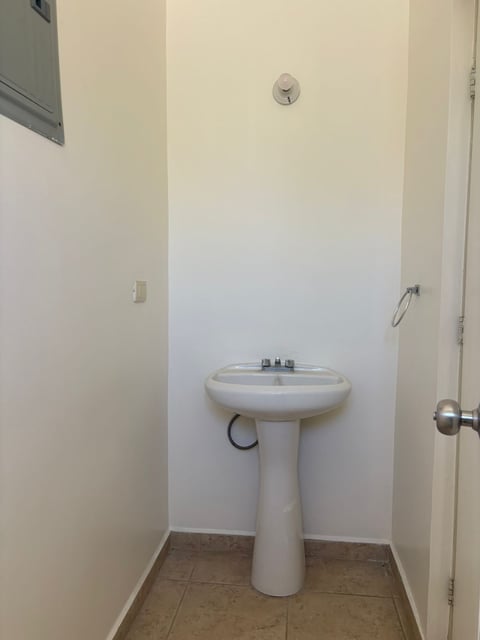 Baño pequeño con lavamanos tipo pedestal, foco en pared y piso de loseta café