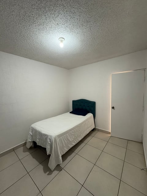 Recámara minimalista con cama individual, edredón blanco y cabecera oscura