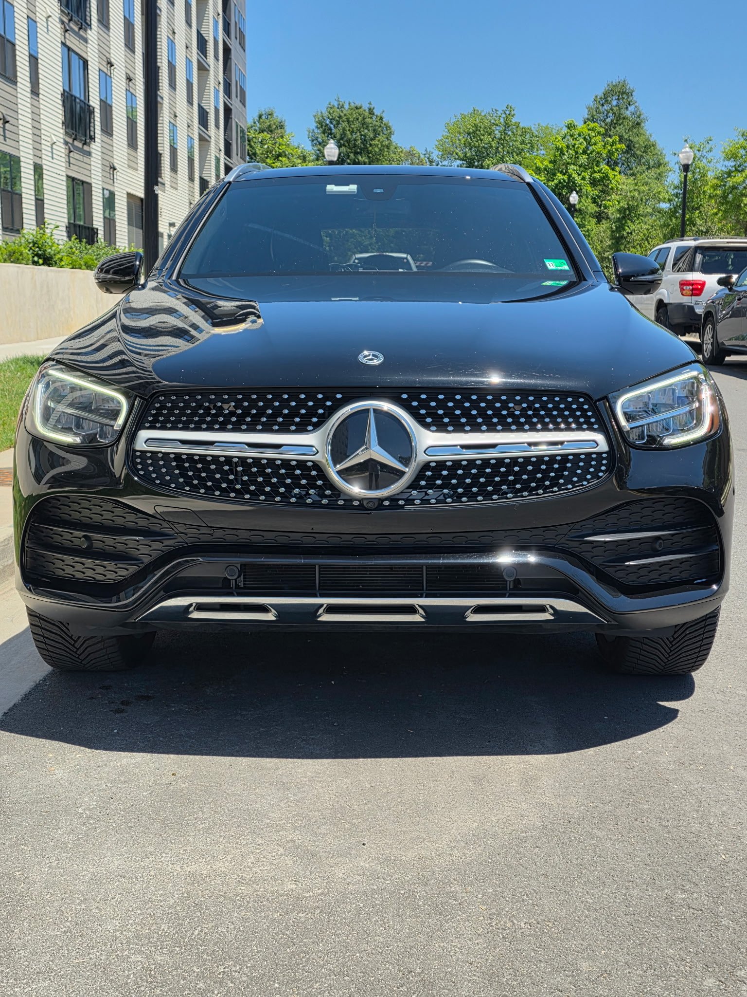 Black Mercedes-Benz SUV parked in front of a building with trees in the background on a sunny day