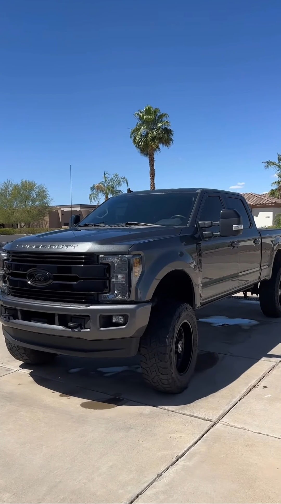 Dark blue Ford Super Duty pickup truck parked on a driveway on a sunny day with palm trees in the background