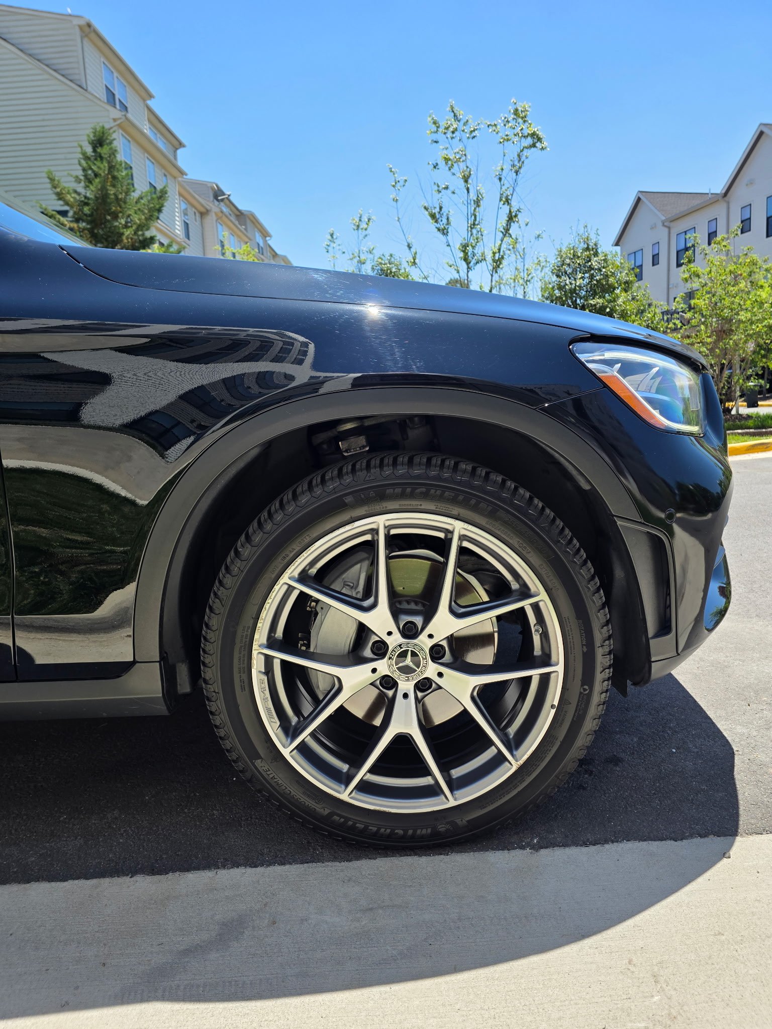Close-up of black SUVs front wheel and fender, showing silver alloy wheel and tire on residential street