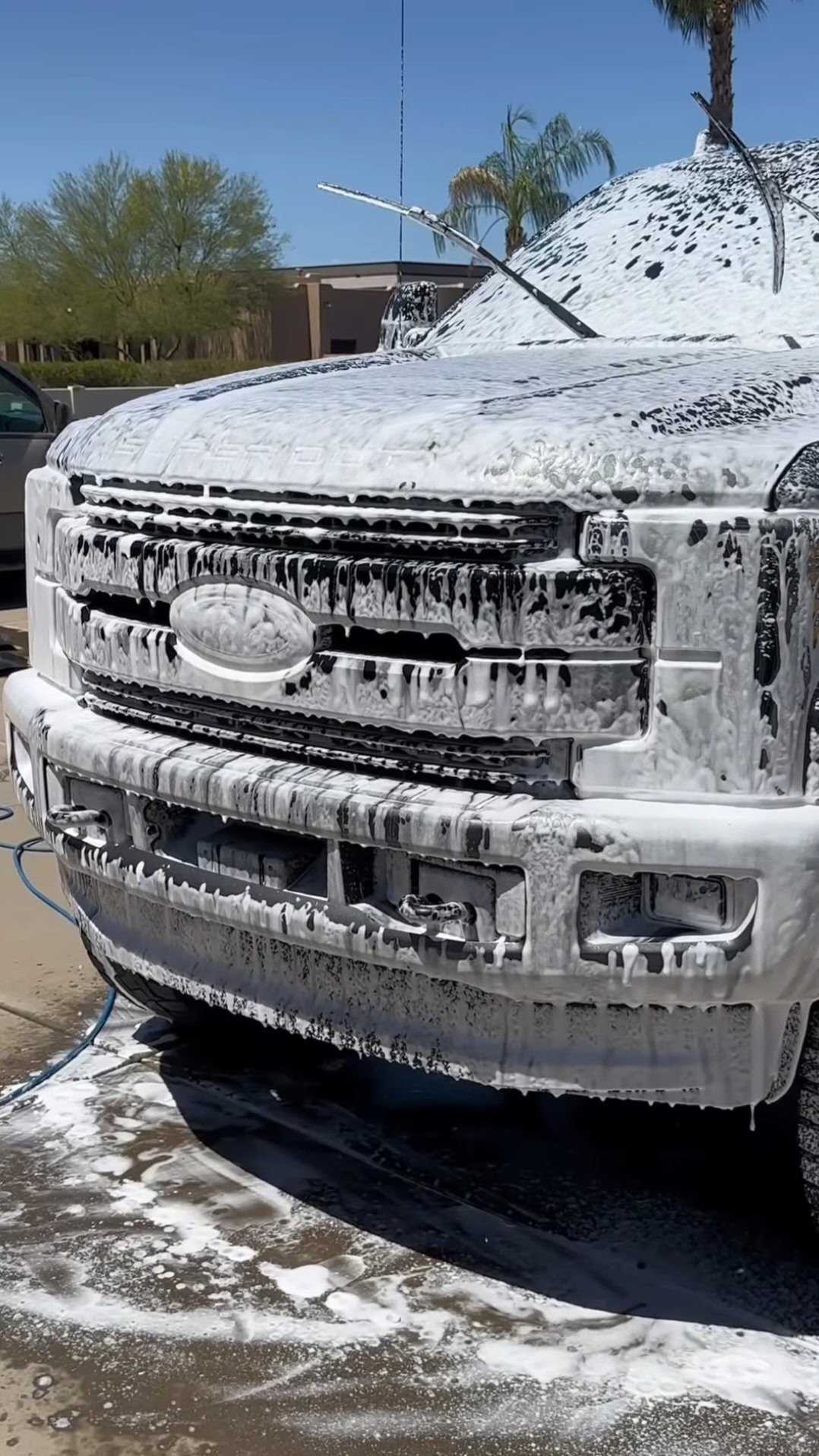 Pickup truck covered in soap suds and foam during a car wash, with mountains and palm trees visible in the background