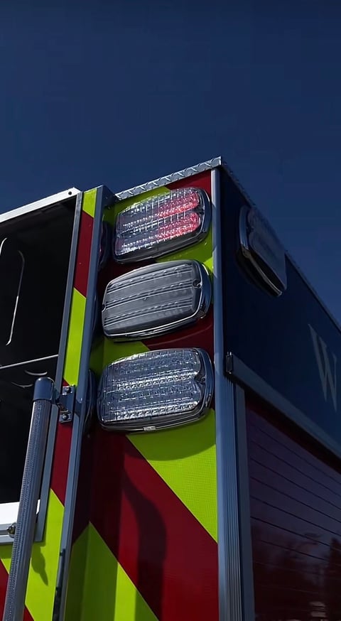 Close-up of emergency vehicle tail lights with neon yellow and red chevron reflective striping against a blue sky