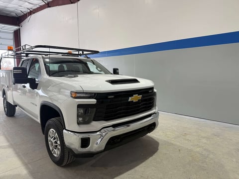 White Chevrolet Silverado pickup truck with roof rack parked in industrial garage with blue stripe on wall