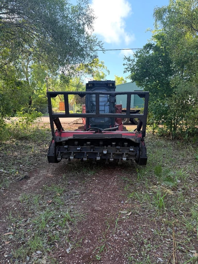 Rear view of a black agricultural harvester machine on a dirt road surrounded by trees and vegetation under blue sky