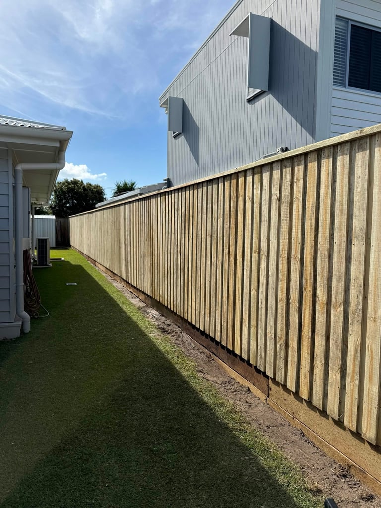 Residential backyard with corrugated metal fence, green lawn, and modern house exterior on clear day