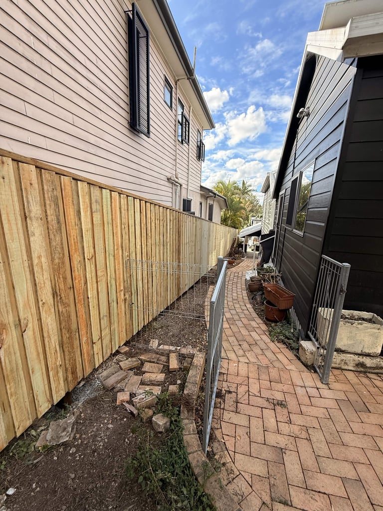 Narrow residential side passage between two houses with brick paving, wooden fence, and metal gate