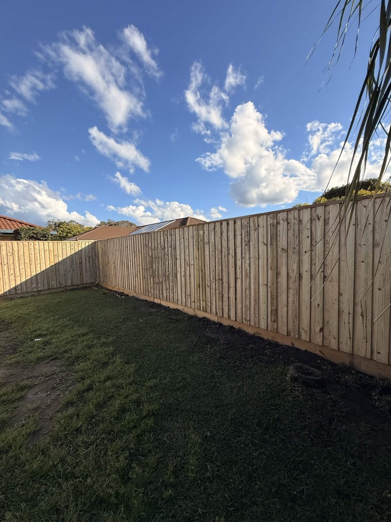 Backyard with wooden fence, green grass, and blue sky with white clouds