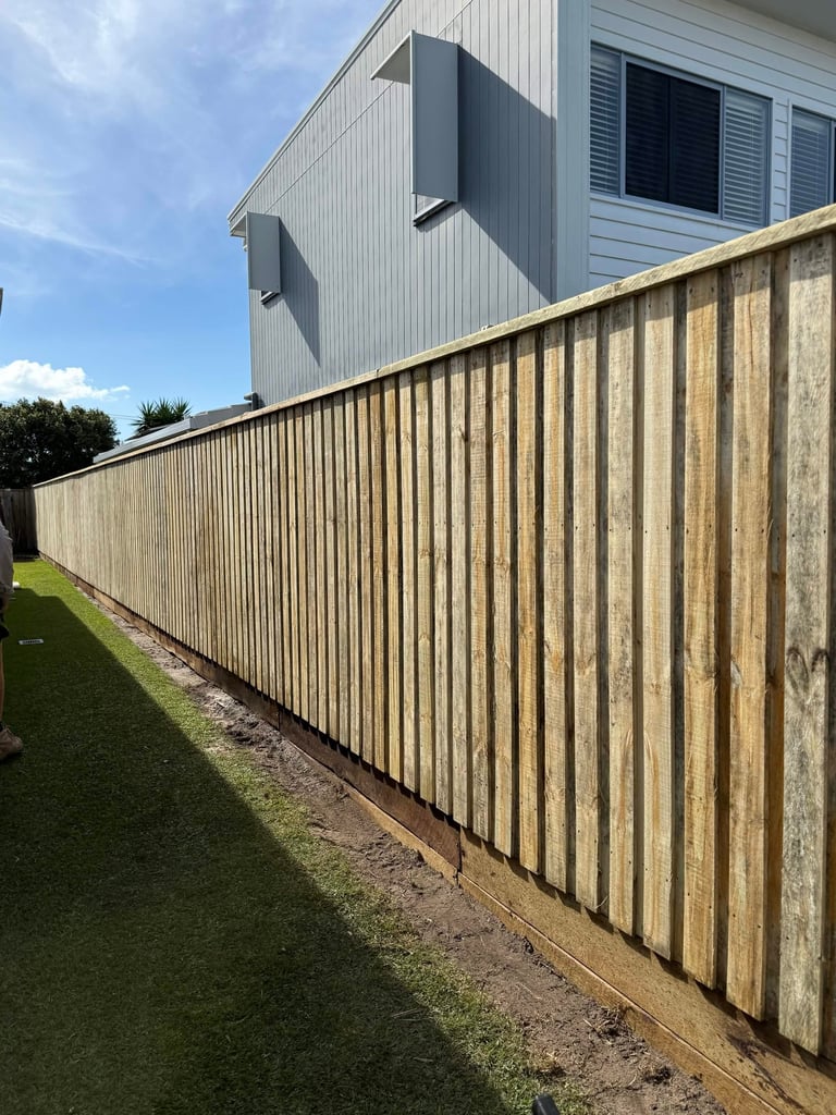 Wooden vertical slat fence bordering a green lawn with a modern house and blue sky in the background