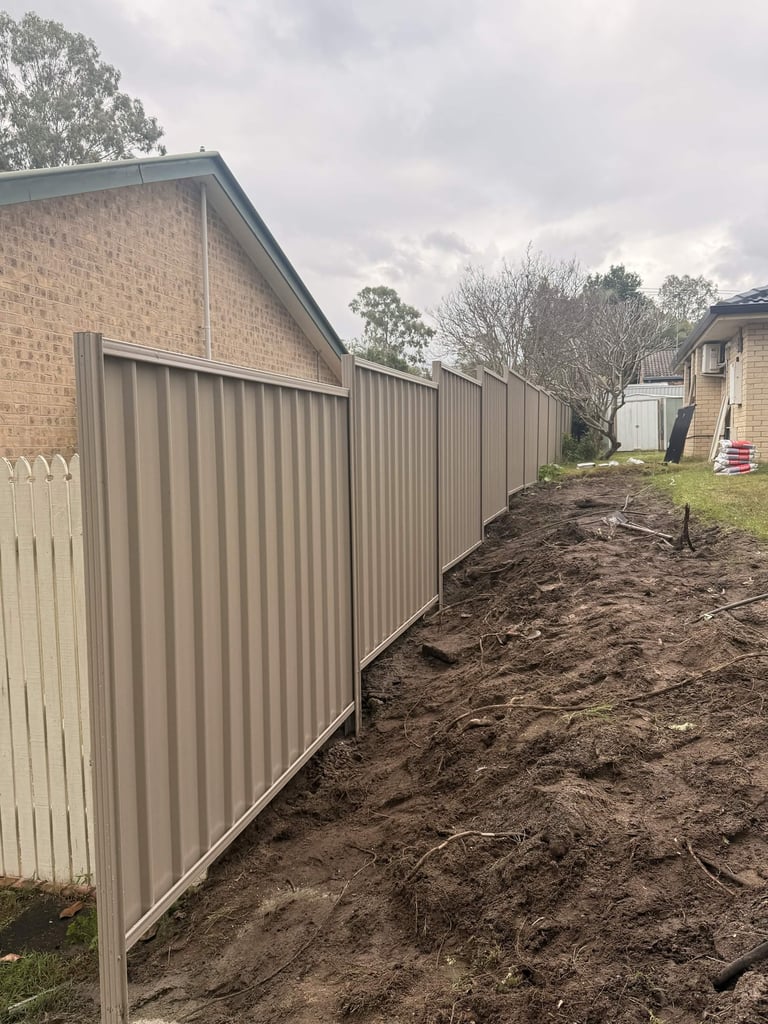 Metal corrugated fence under construction beside brick residential buildings and bare ground