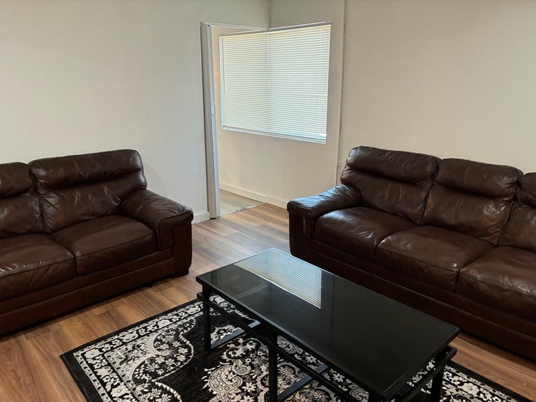 Cozy living room with two brown leather sofas facing a black glass coffee table — a comfortable place to relax and connect