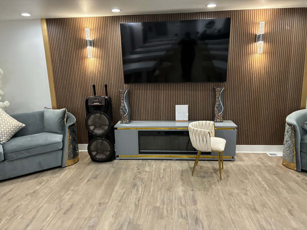 Comfortable living room with gray armchairs, wall-mounted TV, wood accent wall, media console, and speakers — perfect for relaxation, music, and conversation