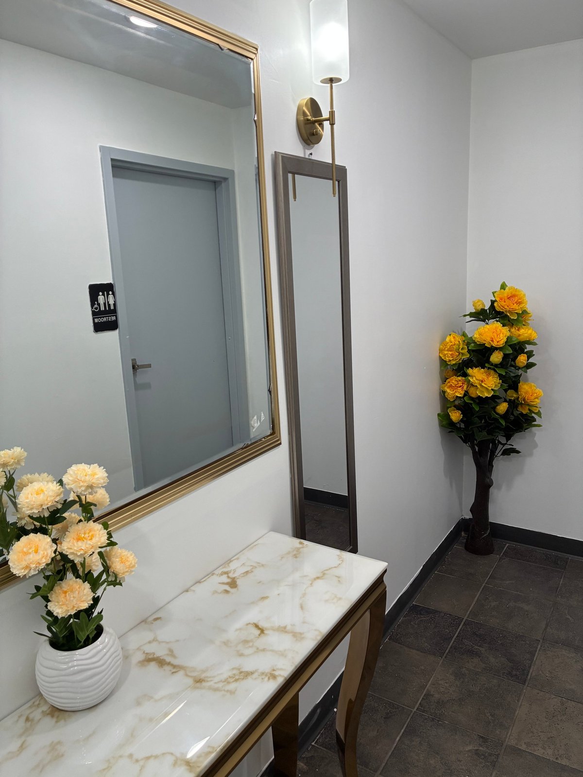 Elegant bathroom with marble vanity, gold-framed mirror, fresh flowers, and minimalist decor — every space, even the smallest, is cared for