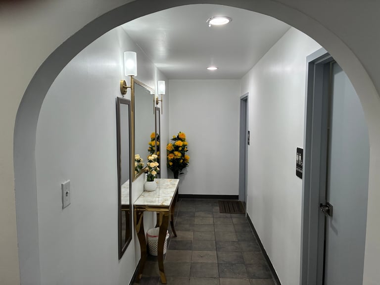 Another view of our elegant hallway with arched entrance, console table with yellow flowers, and wall sconces