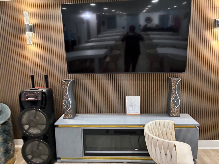 Entertainment area with mounted TV, warm wood accent wall, speakers, and karaoke setup for music, movies, and fun