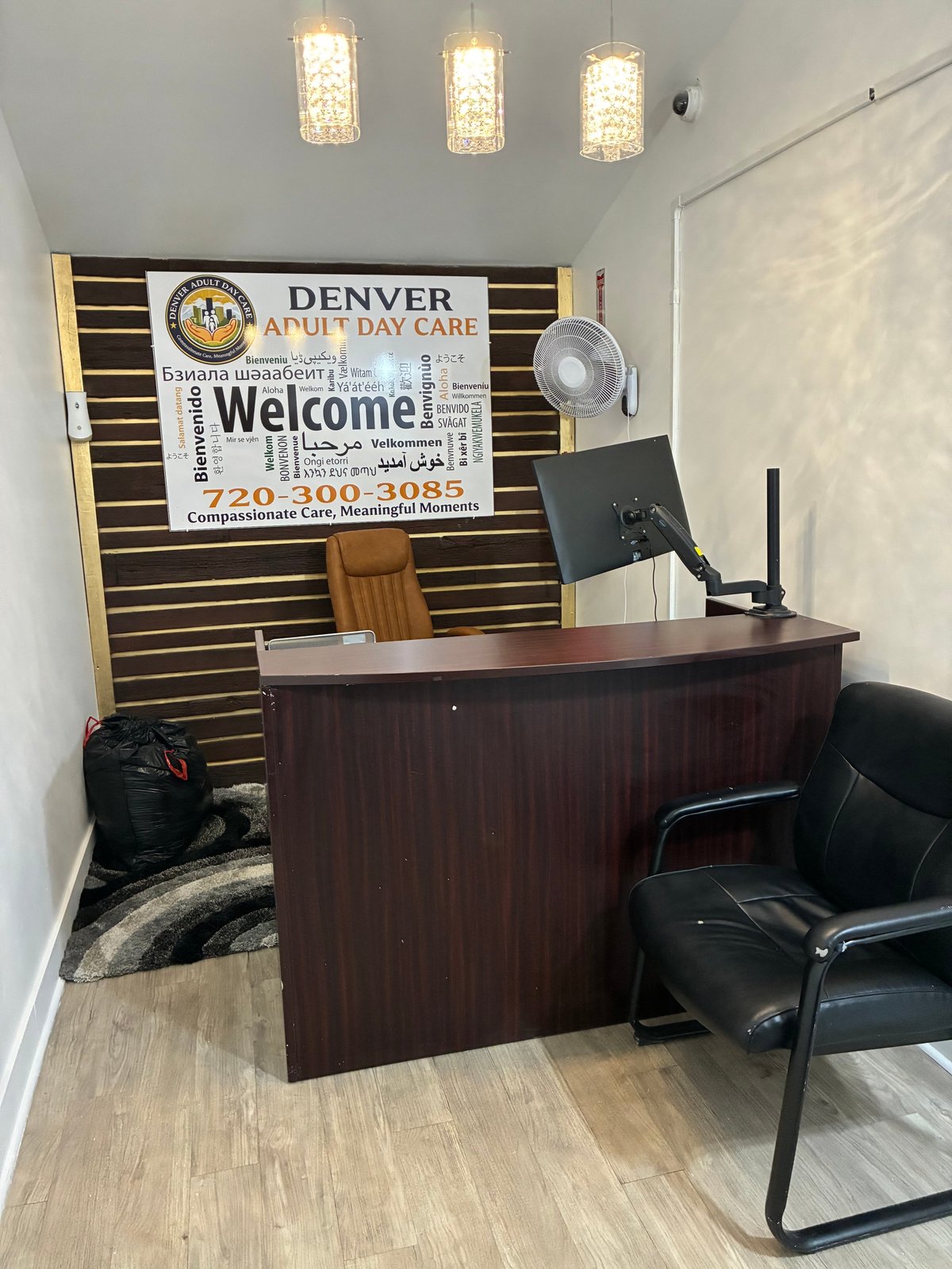 Denver Adult Day Care reception desk with a welcome sign in many languages and the tagline 'Compassionate Care, Meaningful Moments'