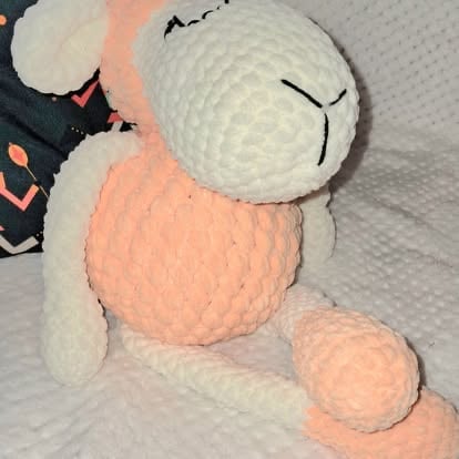 Soft crocheted or knitted plush toy with white head and pink body parts, featuring closed eyes and simple embroidered details