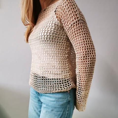Woman wearing a cream crochet open-knit sweater over a light blue jeans, shown from the side