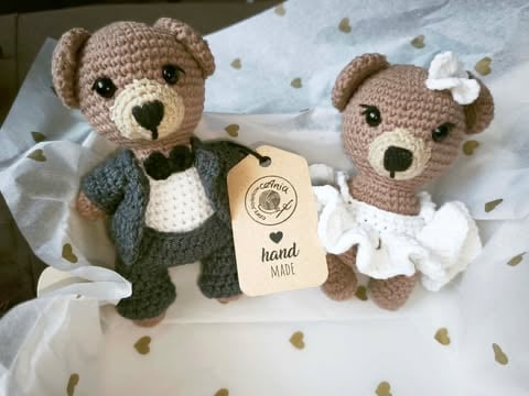 Two handmade crocheted teddy bears with a hand-made label, displayed on white fabric with decorative hearts