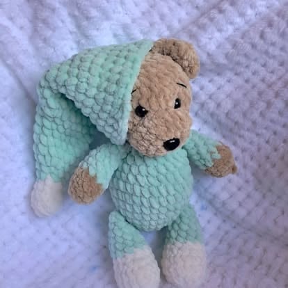 Handmade crocheted stuffed bear toy wearing a mint green sweater and hat on white textured background