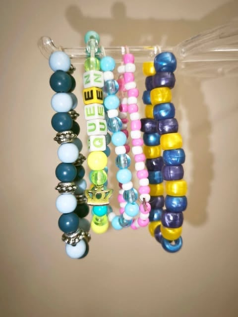 Six colorful beaded bracelets hanging on a jewelry organizer with varied beads in blue, pink, yellow, and white tones