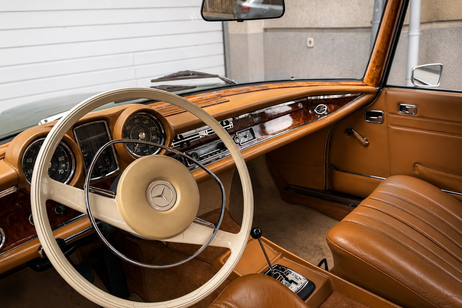 Classic car interior featuring a tan and brown leather cabin with a steering wheel, dashboard, and vintage controls in a garage