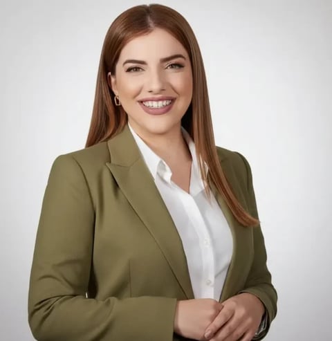 Professional portrait of a smiling woman with long brown hair wearing an olive green blazer and white blouse against a neutral background