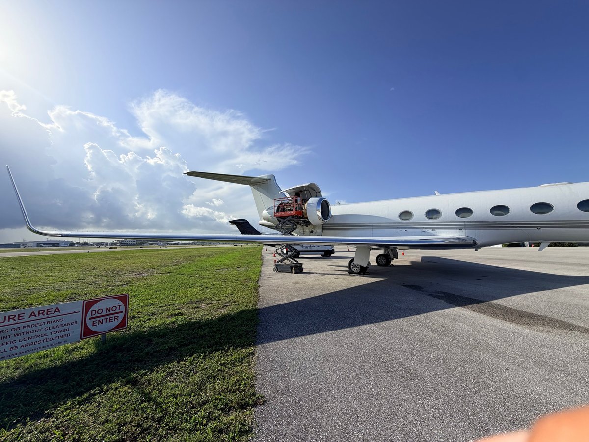 Large private jet parked on tarmac beside green grass area under blue sky with white clouds