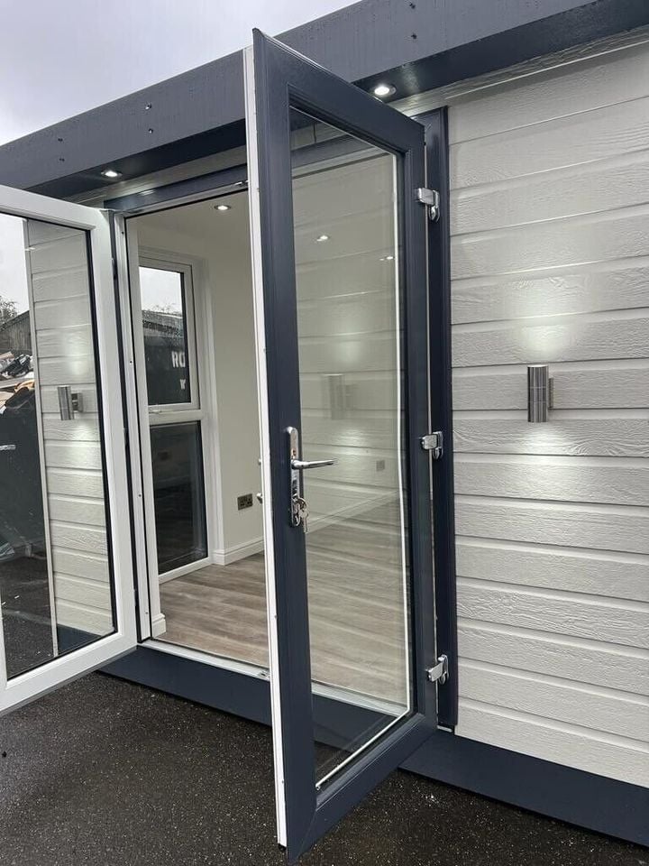 Modern modular building entrance with dark frame door, white textured walls, and interior lighting visible through glass panels