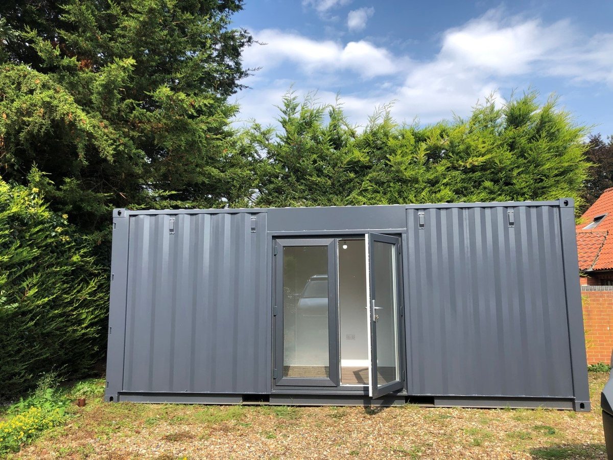 Modern gray shipping container structure with glass door and windows set in landscaped garden