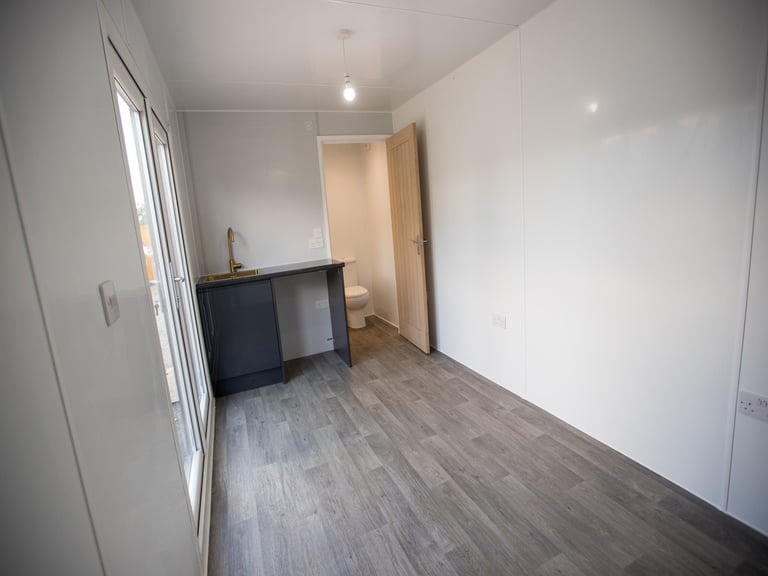 Empty bedroom with wooden flooring, white walls, dark desk, and open door leading to hallway