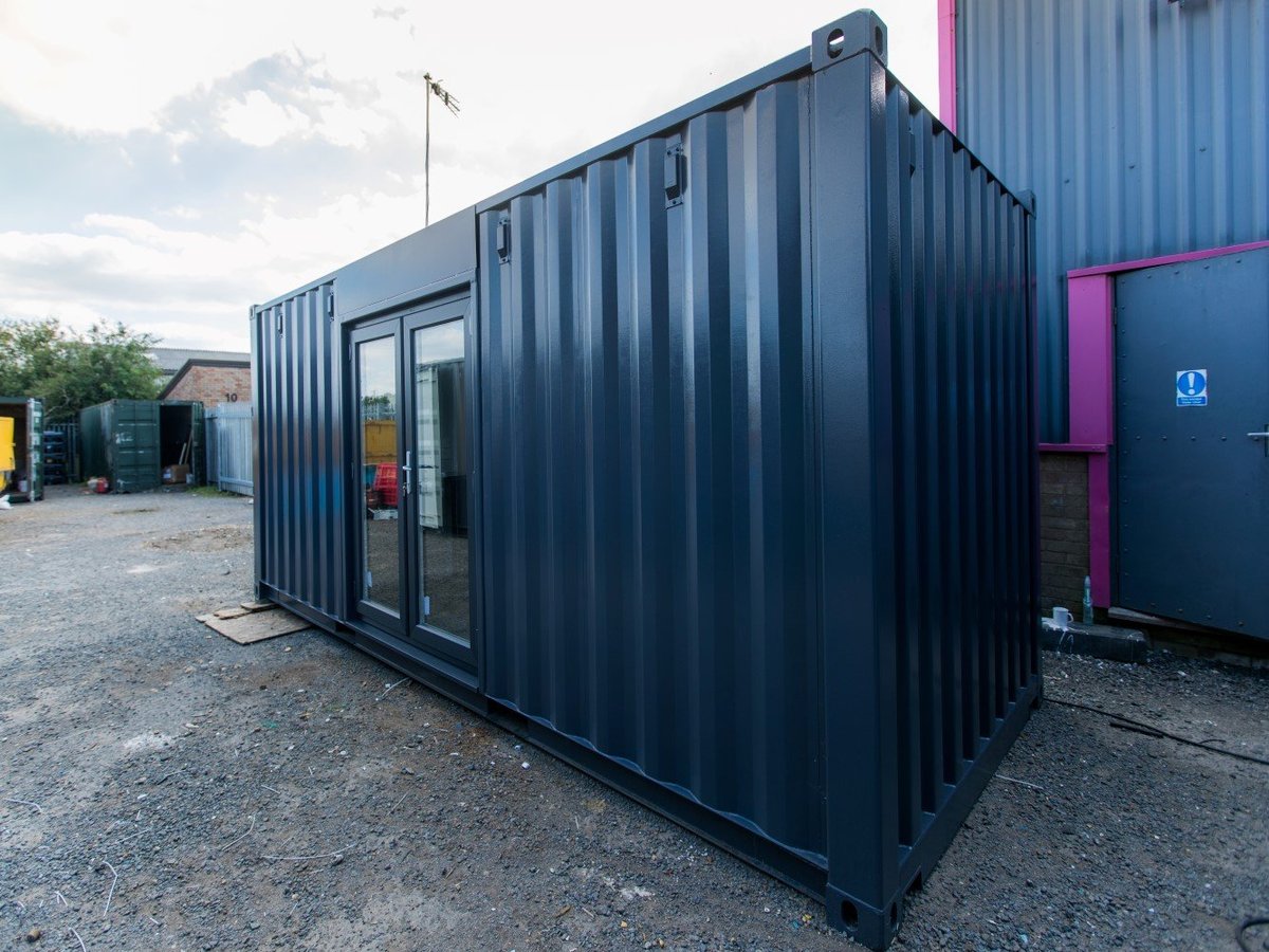 Modern black shipping container converted into a small office or mobile workspace with windows and a door