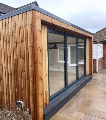 Modern wooden garden room extension with large black-framed sliding glass doors and patio access