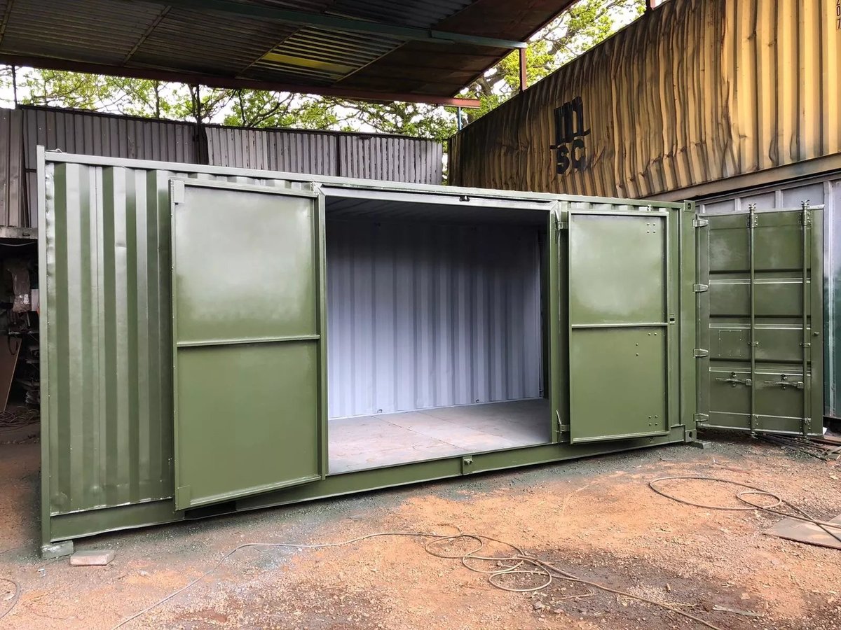Green shipping container storage unit with open doors revealing white interior, set under a metal roof structure