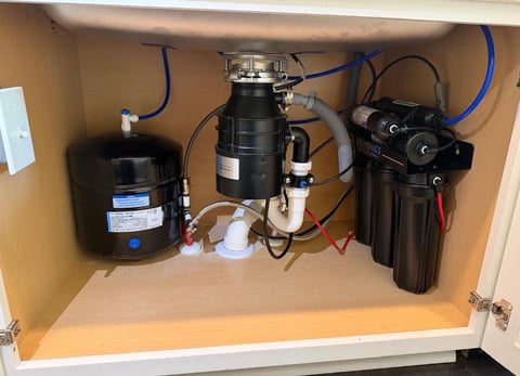 Under-sink water filtration system with pressure tank, garbage disposal unit, and filter cartridges installed in kitchen cabinet.