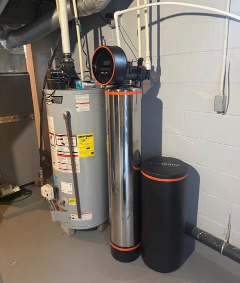 Water softener system with cylindrical tanks and orange-trimmed equipment mounted in a basement utility area.