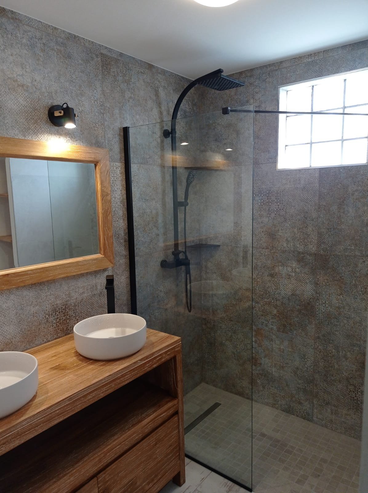 Modernes Badezimmer mit Holzwaschtisch, weißem Aufsatzwaschbecken, gerahmtem Spiegel, großer Glasduschabtrennung und grauen Fliesenwänden
