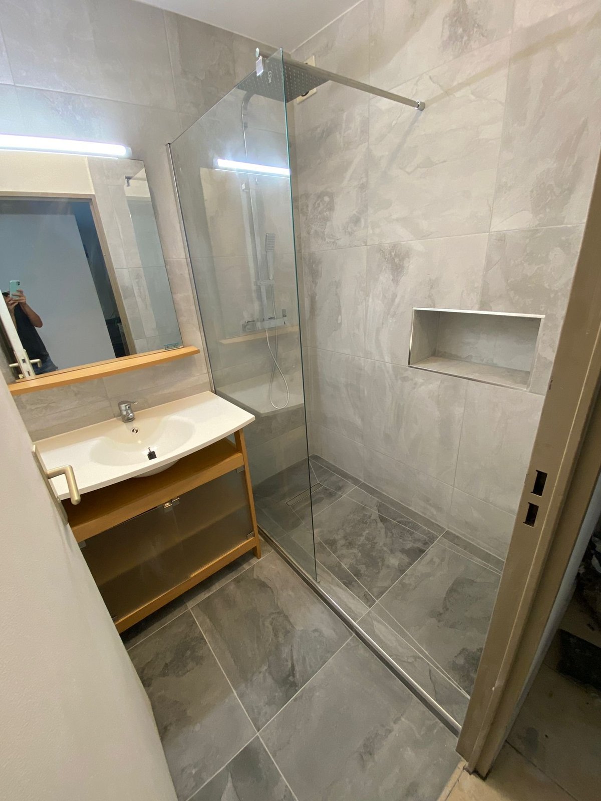Modernes Badezimmer mit Holzwaschtisch, rechteckigem Spiegel und bodengleicher Walk-in-Dusche mit Glasabtrennung und grauen Fliesenwänden