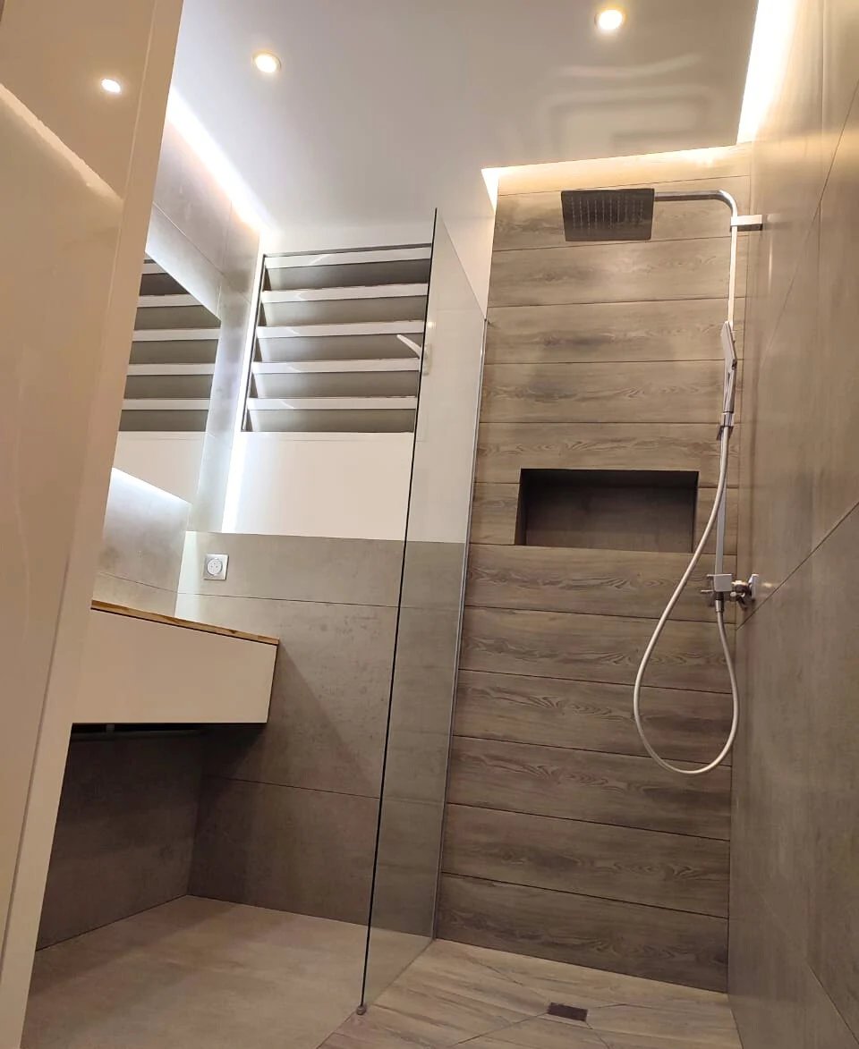 Modern bathroom with walk-in shower featuring gray wood-look tile walls, glass panel, showerhead, and recessed ceiling lighting