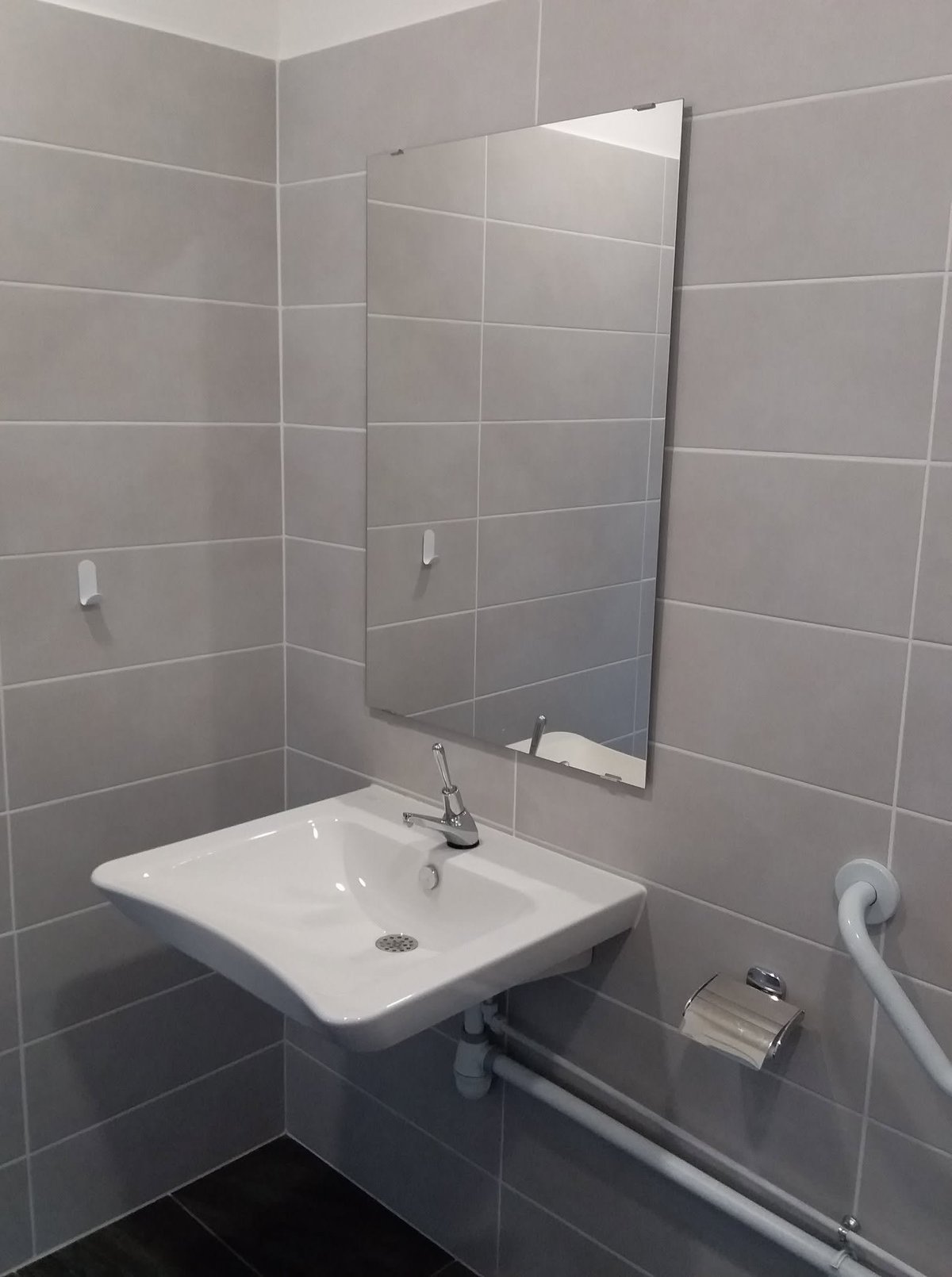 Modern bathroom with gray tiled walls, white rectangular sink, mirror, faucet, and white grab bars