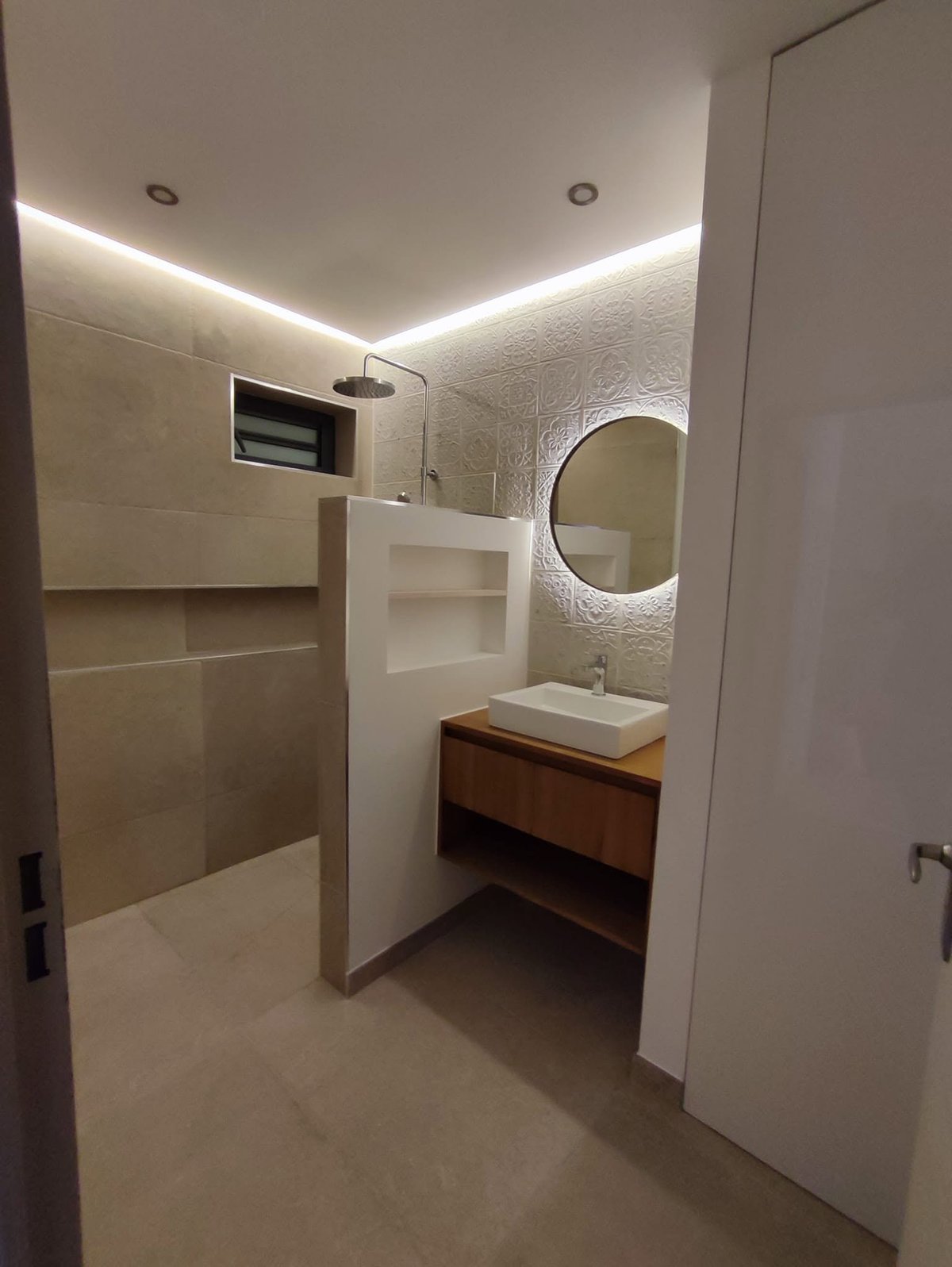 Modernes Badezimmer mit weißen Fliesenwänden, indirekter LED-Deckenbeleuchtung, rundem Spiegel, Holzwaschtisch und Walk-in-Dusche mit Glasabtrennung