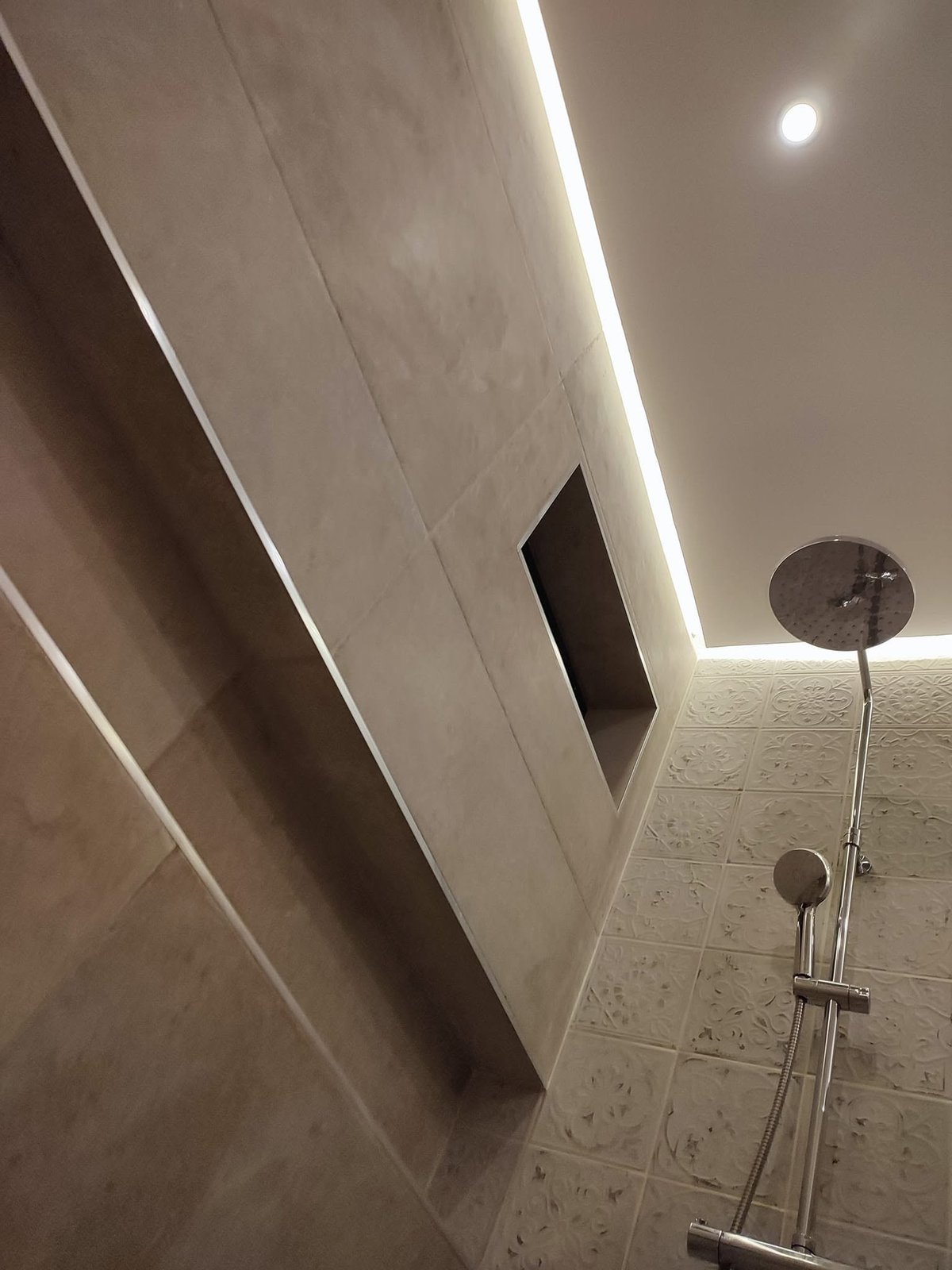 Moderne Duschkabine mit geschwungener Milchglaswand, LED-Lichtband, Chrom-Regenbrause und Handbrause an strukturierter Fliesenwand
