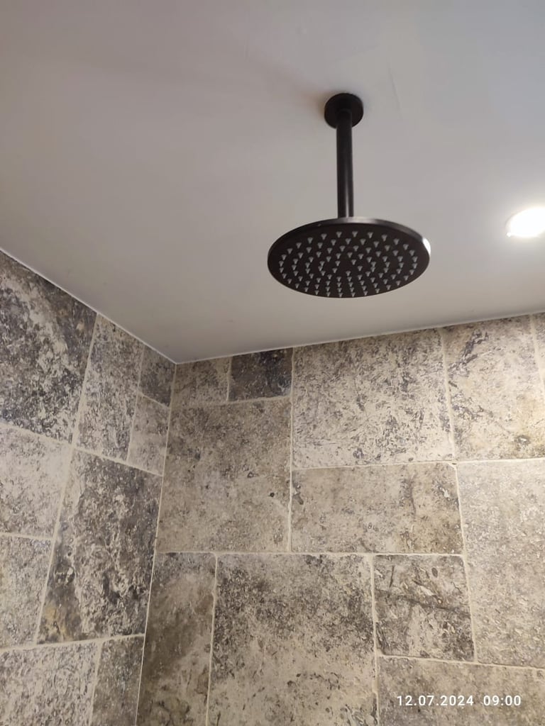 Black ceiling-mounted rainfall showerhead with round nozzle in modern bathroom with gray stone tile walls