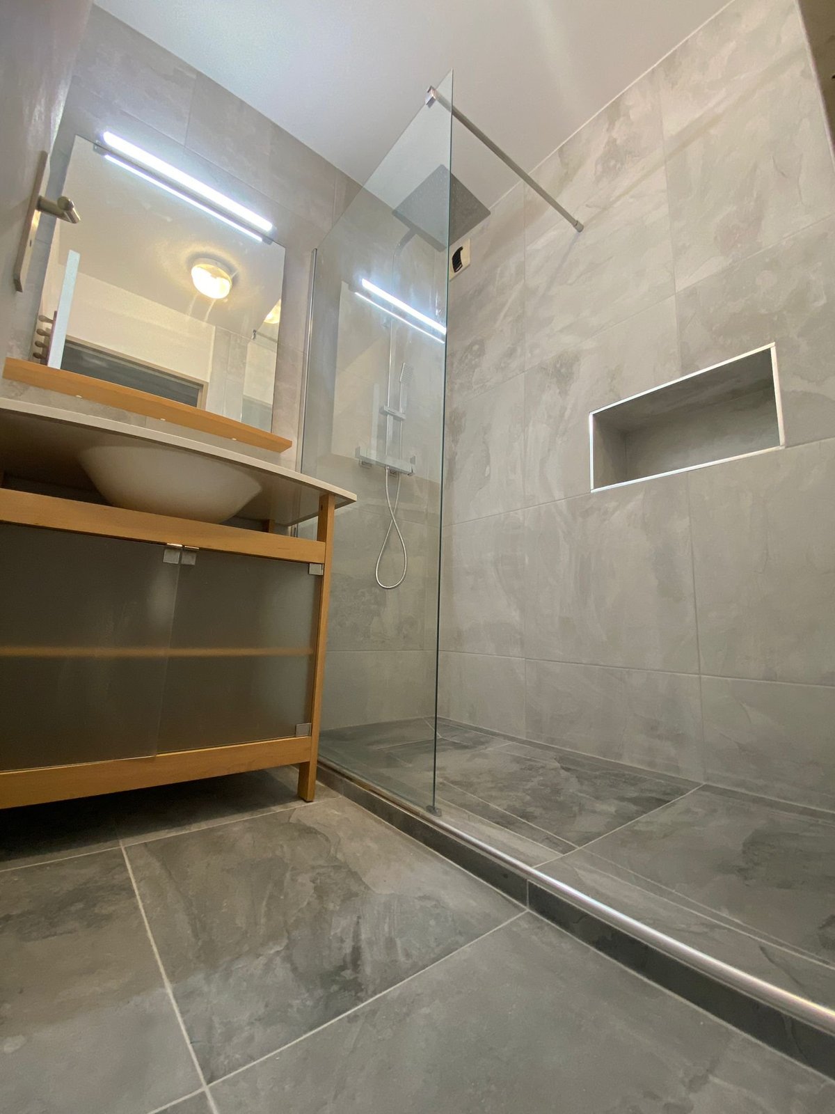 Modernes Badezimmer mit Walk-in-Dusche, grauen Fliesen, Holzwaschtisch mit Aufsatzwaschbecken und großem Spiegel
