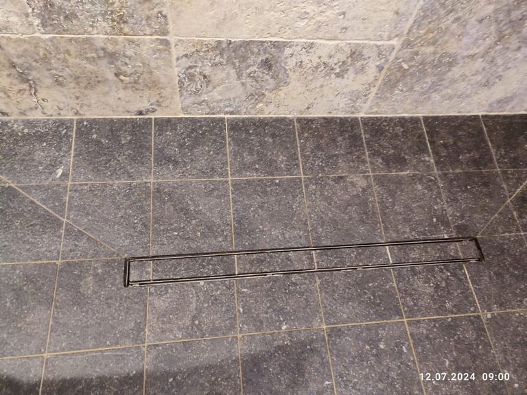 Metal towel bar lying on tiled floor with light and dark gray stone tiles