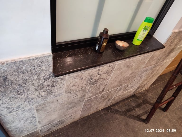 Bathroom vanity with mirror featuring black trim, granite countertop, and various toiletries and products displayed on the ledge