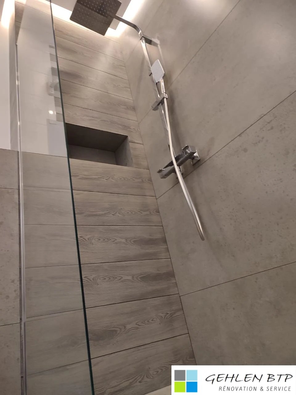 Modern bathroom shower with glass partition, wood-grain tile walls, chrome fixtures, and overhead rain showerhead