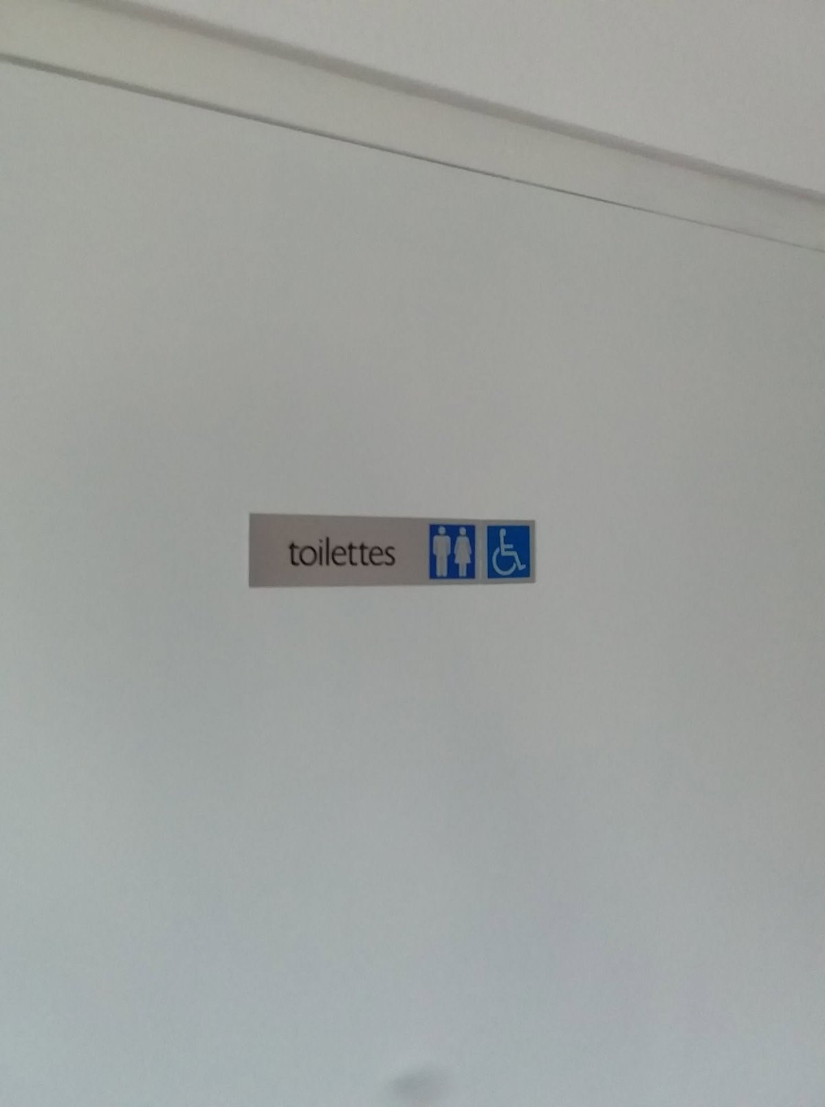 A restroom sign mounted on a white wall with the word toilettes and male, female, and wheelchair accessibility icons