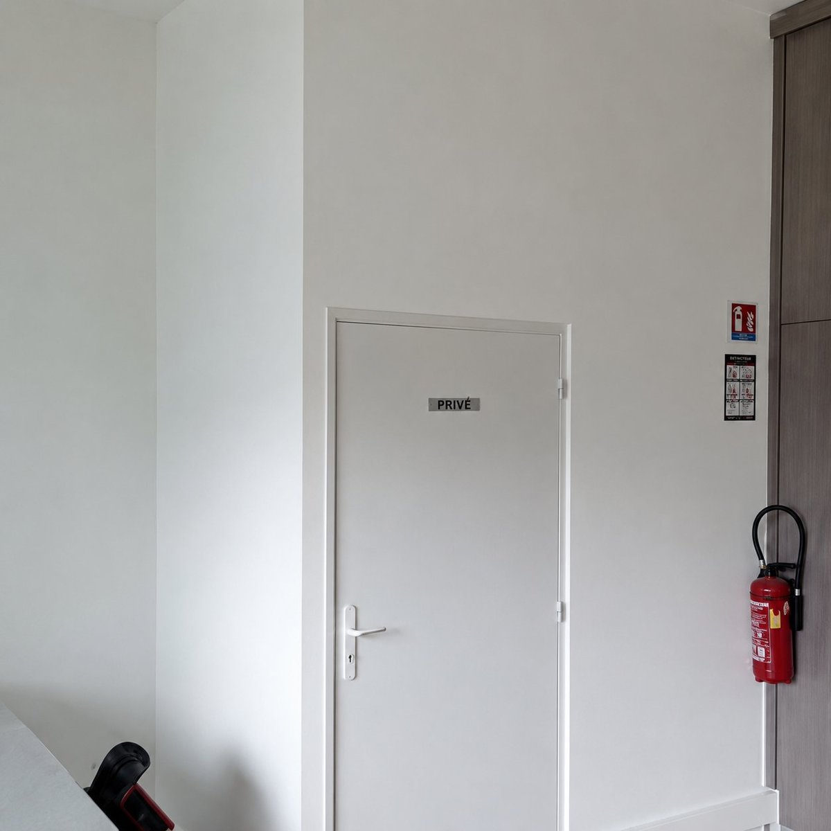 Sauberer Flur mit weißen Wänden, einer Tür mit Aufschrift Privé, Feuerlöscher und Zutrittskontrollpanel an der rechten Wand