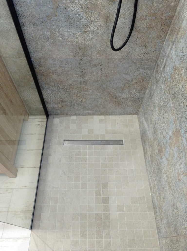 Mosaik — Bodengleiche Dusche mit Linienentwässerung, hellen Mosaik-Bodenfliesen und Steingut-Wandfliesen mit schwarzen Anschlüssen